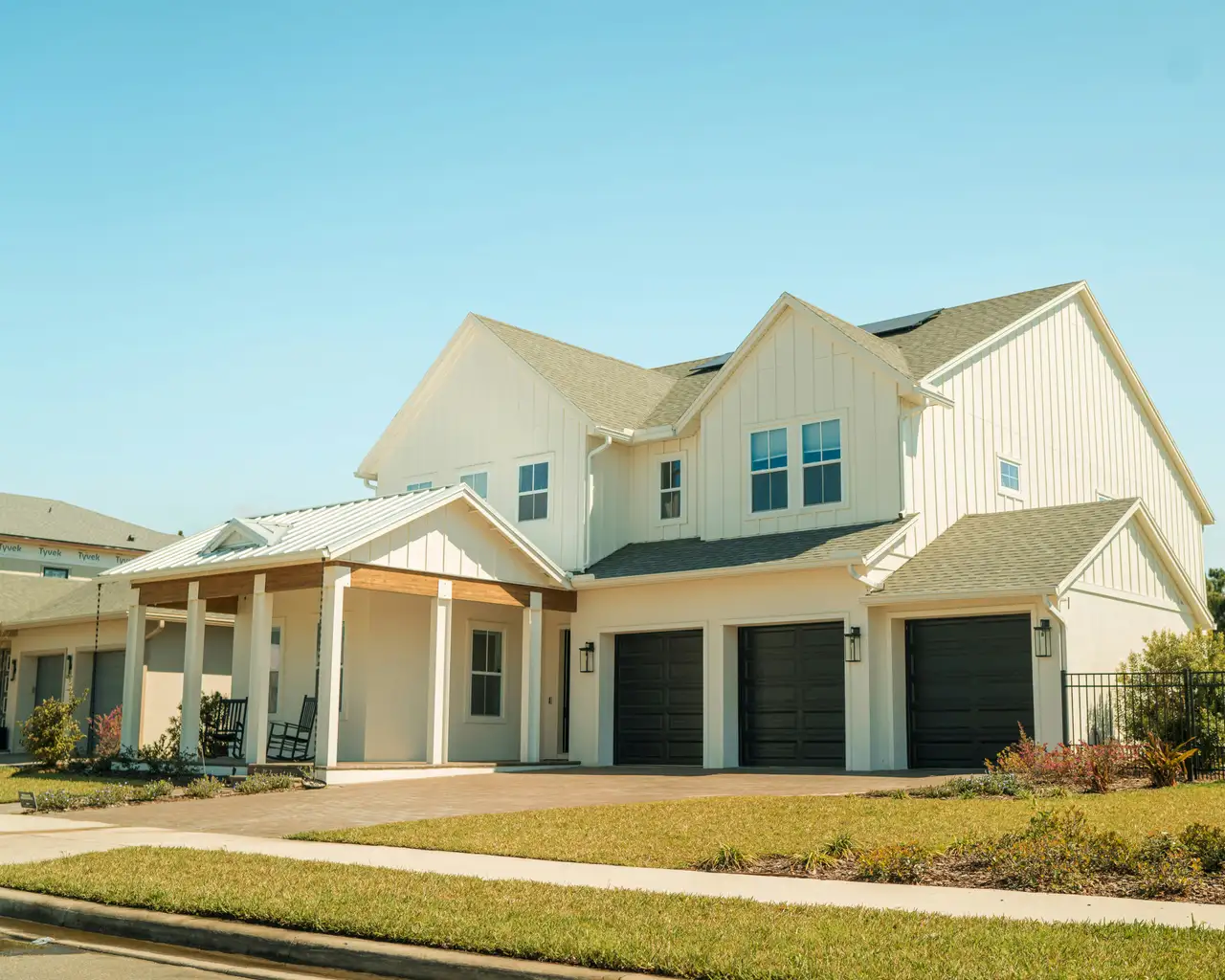 A new two-story modern-farmhouse home with a front porch and three-car garage under a clear Central Florida sky.
